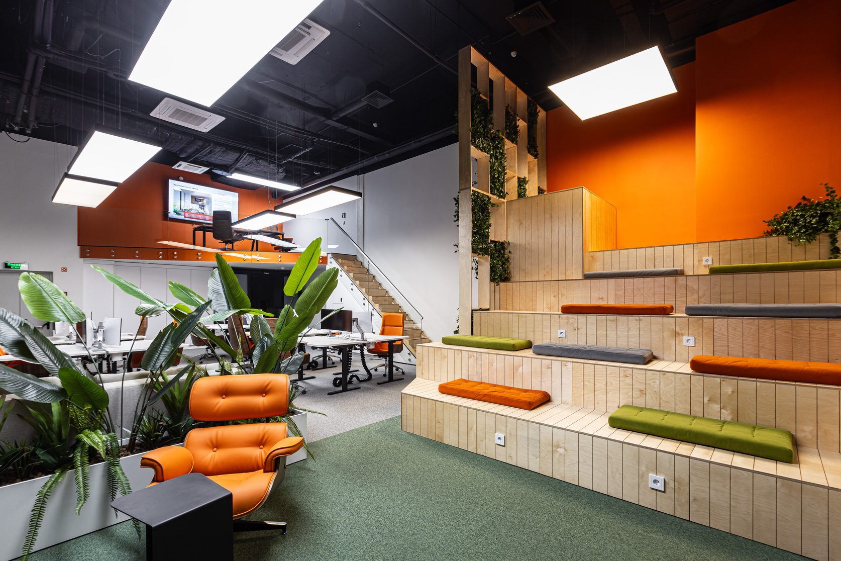 Collaborative call center office with open desks, tiered wooden seating, plants, and orange accent walls
