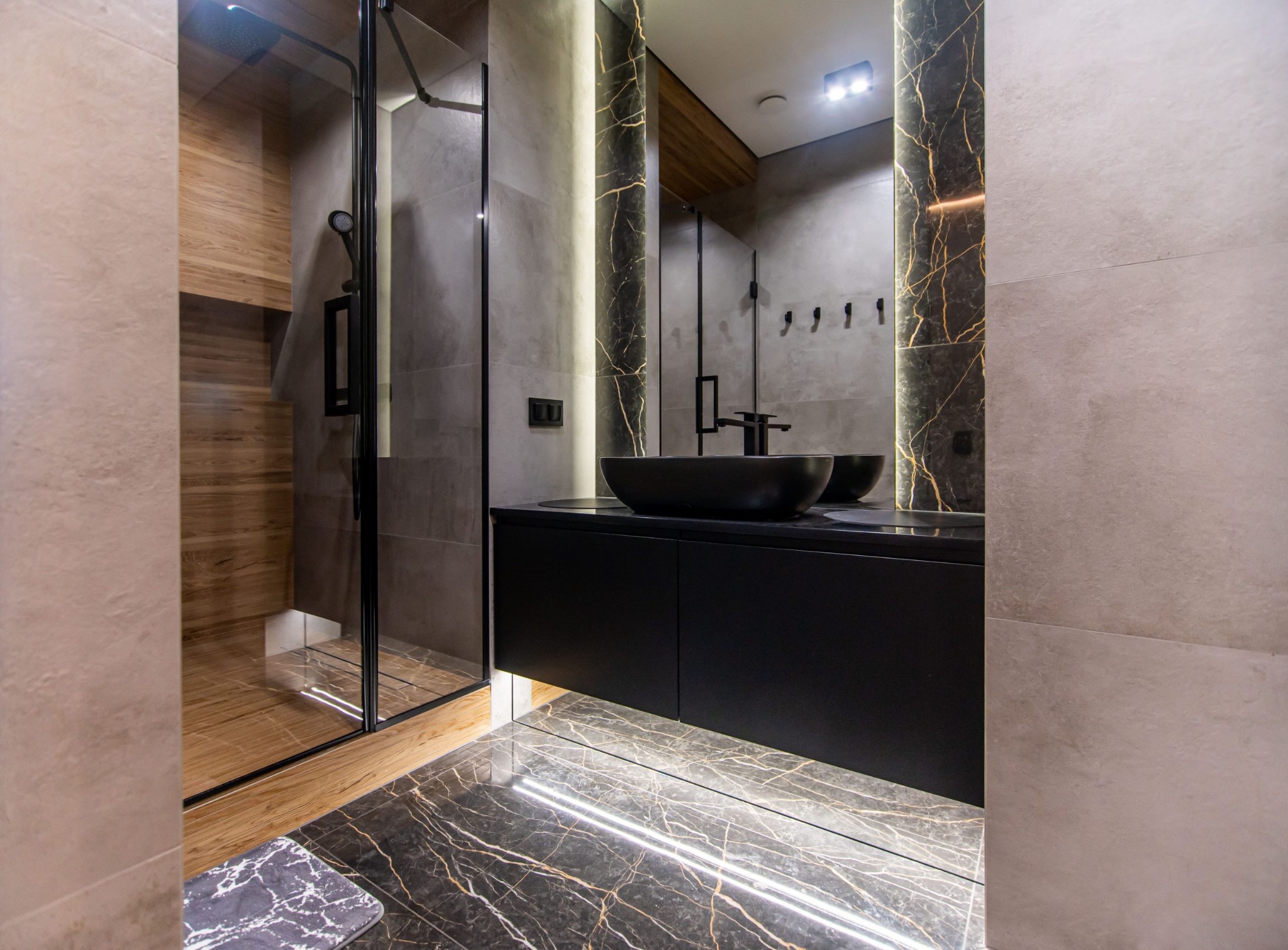 Dark veined stone, wood accents, and concealed lighting frame a floating basin.