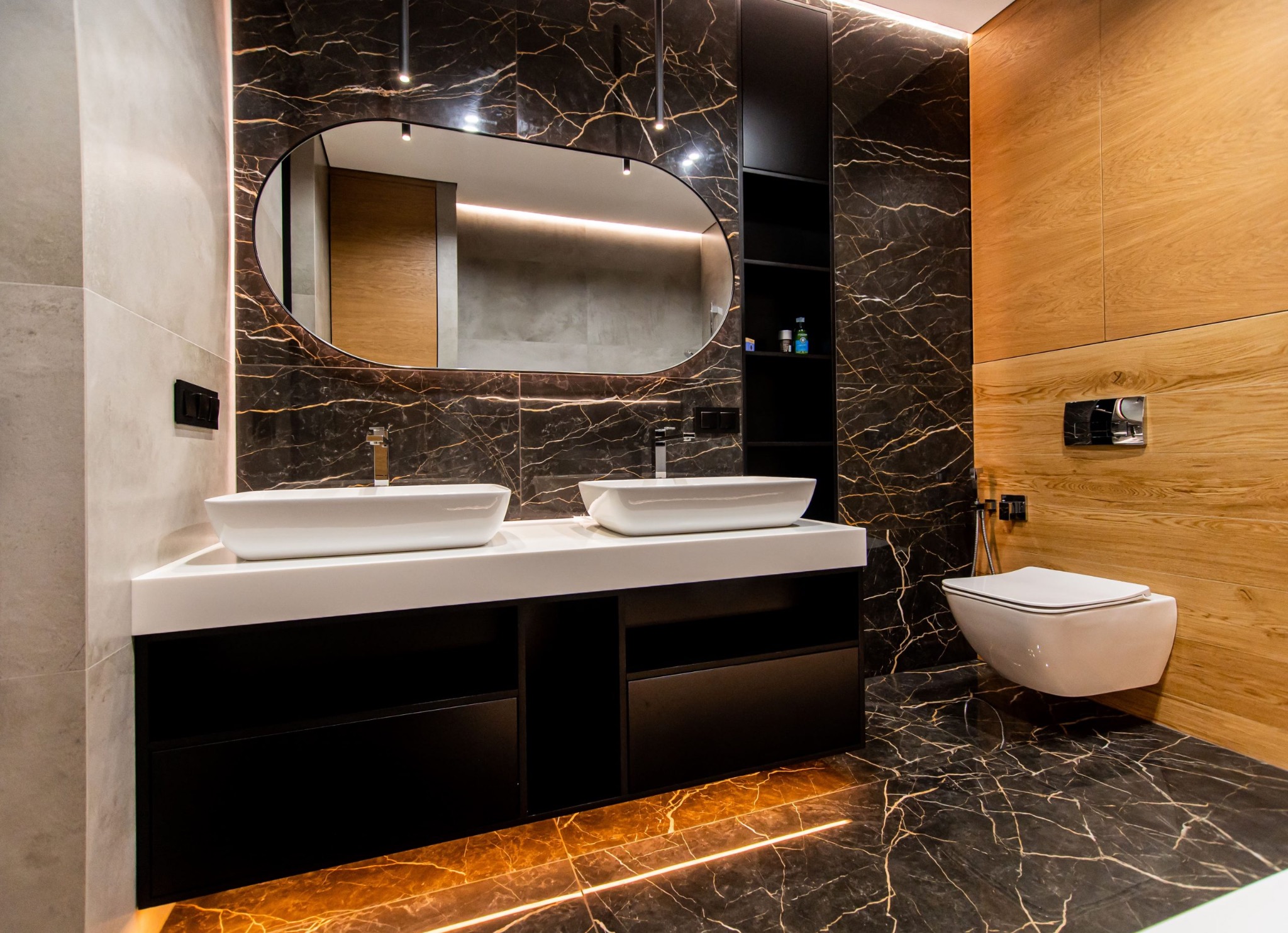 Double vanity with dark veined surfaces, wide mirror and warm lighting